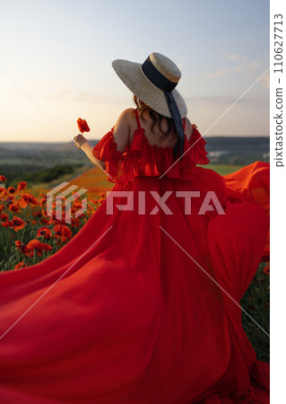 Woman poppy field red dress hat. Happy woman in a long red dress in a beautiful large poppy field. Blond stands with her back posing on a large field of red poppies. 110627713
