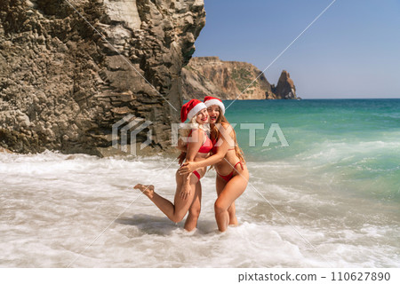 Women in Santa Claus hats run into the sea dressed in red swimsuits. Celebrating the New Year in a hot country Women in Santa Claus hats run into the sea dressed in red swimsuits. Celebrating the New Year in a hot country 110627890