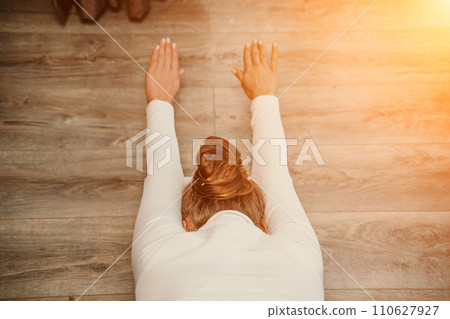 Adult athletic woman, in white bodysuit, performing fascia exercises on the floor - caucasian woman using a massage foam roller - a tool to relieve tension in the back and relieve muscle pain - the 110627927