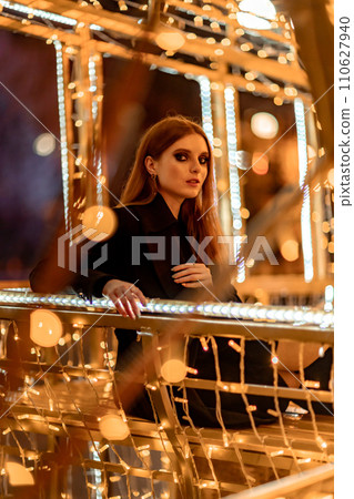 Christmas mood. Woman with long hair in sity decorated for Christmas. She is dressed in a black coat. Christmas mood. Woman with long hair in sity decorated for Christmas. She is dressed in a black coat. 110627940