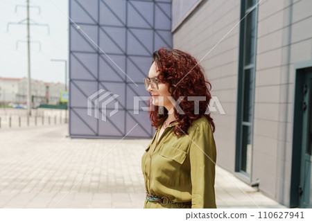 Portrait of a woman standing near a supermarket building. Caucasian model with long brunette hair, wears sunglasses and a khaki dress. Portrait of a woman standing near a supermarket building. Caucasian model with long brunette hair, wears sunglasses and a khaki dress. 110627941