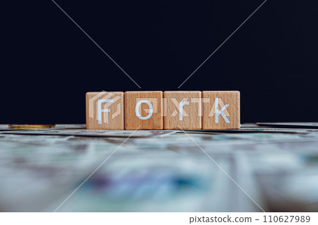 Wooden blocks with the text "Fork" on a black background and crypto banknotes scattered on the ground. 110627989