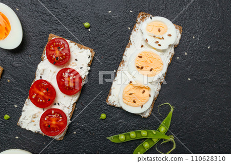 Ingredients for sandwich with boiled egg, cherry tomatoes, canned tuna, garlic and spices over black grunge background. Top view Ingredients for sandwich with boiled egg, cherry tomatoes, canned tuna, garlic and spices over black grunge background. Top view 110628310