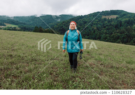 Happy active senior tourist woman listening to music in outdoor leisure trip admiring the landscape feeling inspired by the beauty of nature. 110628327
