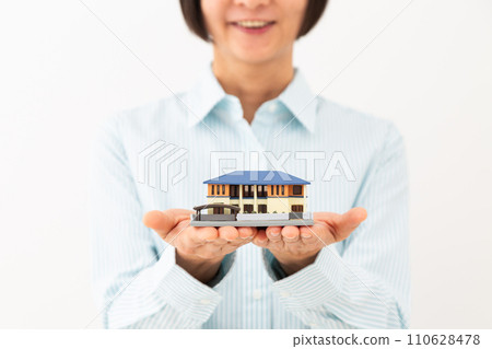 A middle-aged woman smiling while holding a detached house model A middle-aged woman smiling while holding a detached house model 110628478