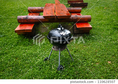 Side View of black BBQ Barbecue grill with cover in home front or backyard and green lawn. Portable BBQ Grill for Outdoor Grill Cooking. 110628507