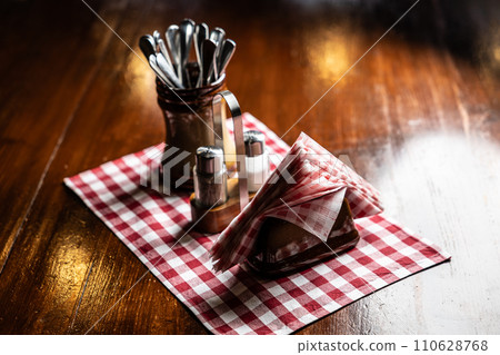 Salt, pepper, napkins and cutlery on a wooden table in a pub or restaurant 110628768