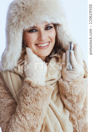 smiling woman in winter coat and fur hat touching face on white 110629508