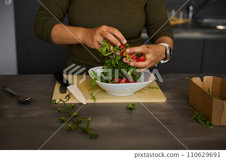 Hands holding fresh green arugula leaves and juicy red tomatoes while preparing healthy raw vegan salad in the home kicthen Hands holding fresh green arugula leaves and juicy red tomatoes while preparing healthy raw vegan salad in the home kicthen 110629691
