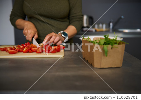 Close-up woman housewife cutting tomatoes, preparing fresh salad, standing at kitchen table Close-up woman housewife cutting tomatoes, preparing fresh salad, standing at kitchen table 110629701