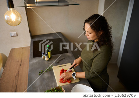 Multiracial young woman chopping vegetables, cooking healthy raw vegan salad for dinner in the kitchen. View from above Multiracial young woman chopping vegetables, cooking healthy raw vegan salad for dinner in the kitchen. View from above 110629709