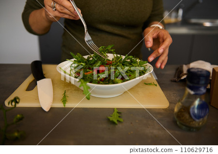 Details on the hands of a woman holding fork and bowl of fresh healthy salad with organic vegetables and greens 110629716