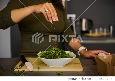 Details on female hand holding salt and seasoning fresh healthy salad while preparing lunch at home kitchen Details on female hand holding salt and seasoning fresh healthy salad while preparing lunch at home kitchen 110629722