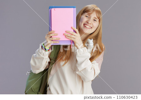 smiling trendy girl with backpack peeking out of notebooks 110630423