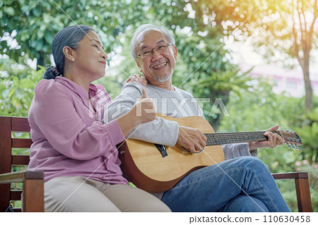 Happy two Asian senior couple elderly man playing the guitar while his wife is singing together at home outdoors, Enjoying lifestyle during retirement life having fun, Activity family health care 110630458