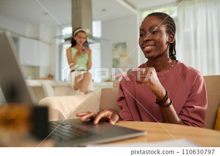 Smiling teenage girl filing nails when watching blog on laptop at home 110630797