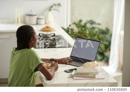 Black girl eating breakfast and watching entertaining video on laptop 110630800
