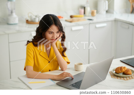 Bored university student sitting at kitchen counter when attending online class 110630860