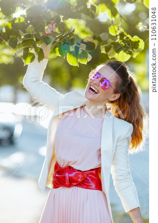 happy trendy female in pink dress and white jacket in city 110631048