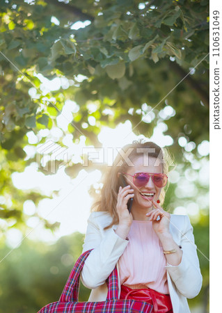 happy woman in dress and jacket in city using smartphone 110631049