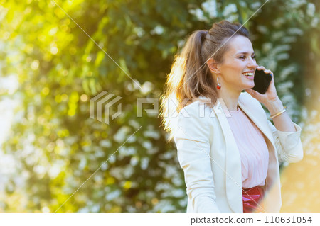 smiling woman in dress and jacket in city talking on phone 110631054