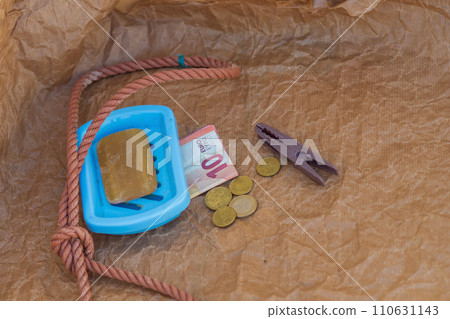 Symbolic scene, solid soap, gallows loop, euro coins, 10 euro banknote, clothespin. Hopeless, lack of earning opportunities, dismissal of employees, replacement of workers with artificial intelligence Symbolic scene, solid soap, gallows loop, euro coins, 10 euro banknote, clothespin. Hopeless, lack of earning opportunities, dismissal of employees, replacement of workers with artificial intelligence 110631143