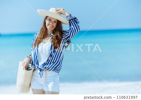 smiling elegant woman on ocean shore with straw bag smiling elegant woman on ocean shore with straw bag 110631997