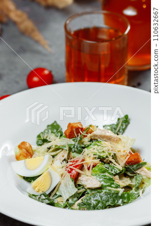 Traditional caesar salad in a white bowl on a old white table with leaves and a sauce boat and parmesan. Selected focus. Traditional caesar salad in a white bowl on a old white table with leaves and a sauce boat and parmesan. Selected focus. 110632667