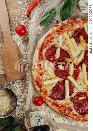 Pizza with chicken cheese and pepperoni, a piece of which is cut and laid out like a pakman, is on a wooden board and a brown background. Cheese spreads flowing streaks 110632678