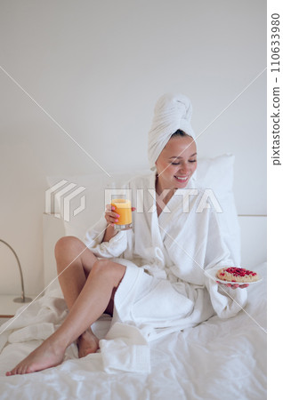 Cute young woman in bath robe having breakfast and feeling enjoyed 110633980