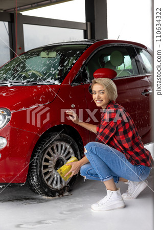 Short-haired blonde woman washing a car and looking contented Short-haired blonde woman washing a car and looking contented 110634322