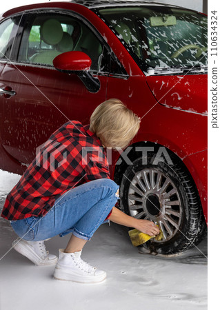 Short-haired blonde woman washing a car and looking contented Short-haired blonde woman washing a car and looking contented 110634324