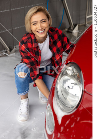 Short-haired blonde woman washing a car and looking contented Short-haired blonde woman washing a car and looking contented 110634327