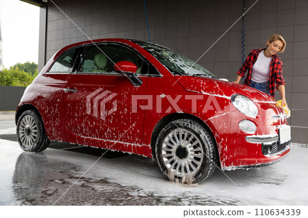 Blonde young woman washing a car and feeling positive 110634339