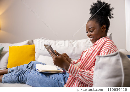Optimistic woman relaxing on sofa using digital tablet scrolling online using internet app. 110634426