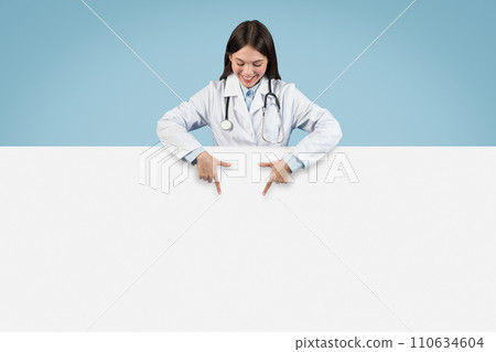 Joyful woman doctor pointing downwards at an empty banner 110634604