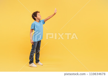 Curious boy reaching out free space in blue shirt on yellow background 110634678