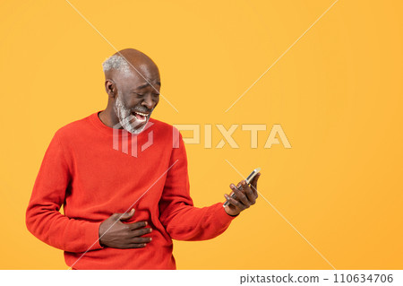 Joyful elderly man in a red sweater laughs while looking at a smartphone Joyful elderly man in a red sweater laughs while looking at a smartphone 110634706