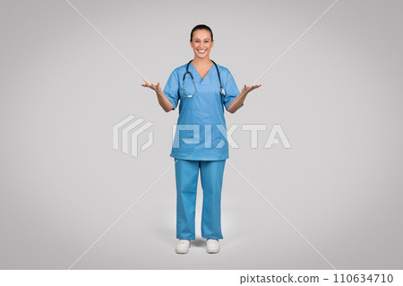 Smiling female doctor wearing blue medical uniform coat and stethoscope talking to camera, explaining and gesturing 110634710