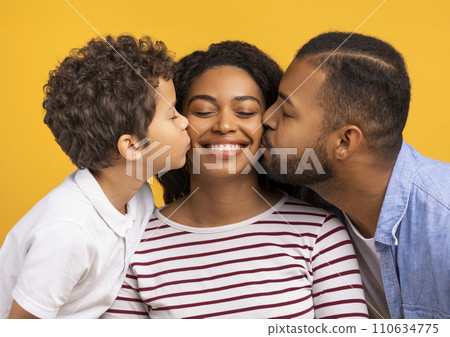 Adorable son and husband giving kisses on cheeks of smiling black mother Adorable son and husband giving kisses on cheeks of smiling black mother 110634775