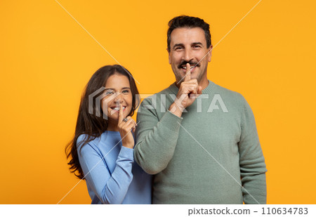 A man and woman in casual clothing smilingly place their fingers on their lips A man and woman in casual clothing smilingly place their fingers on their lips 110634783