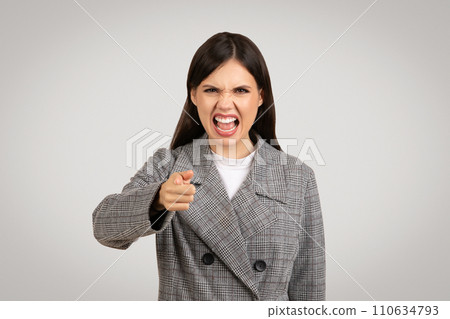 Angry woman in blazer pointing and shouting, frustration evident 110634793