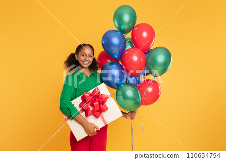 african teenager girl holds bunch of balloons and gift, studio 110634794