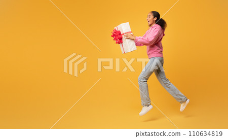 Cheerful African American teen lady offering wrapped present box, studio Cheerful African American teen lady offering wrapped present box, studio 110634819