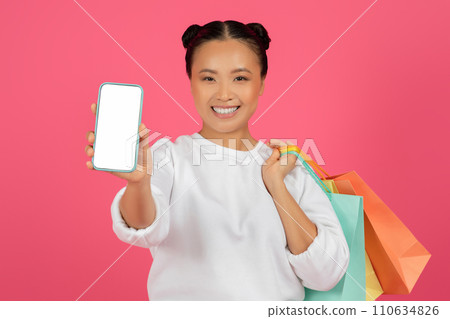 Online Shopping App. Cheerful asian woman demonstrating smartphone with blank white screen 110634826