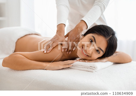 Smiling young indian woman receiving relaxing shoulder massage 110634909