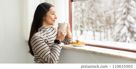 Serene woman in striped turtleneck savoring the taste of her morning coffee 110635003