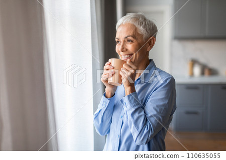 Mature gray lady with haircut sips tea holding cup indoor Mature gray lady with haircut sips tea holding cup indoor 110635055