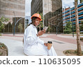 Happy black woman in helmet sitting with coffee cup and browsing smartphone 110635095
