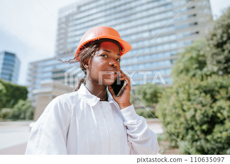 Serious black woman in helmet talking on smartphone in daylight Serious black woman in helmet talking on smartphone in daylight 110635097